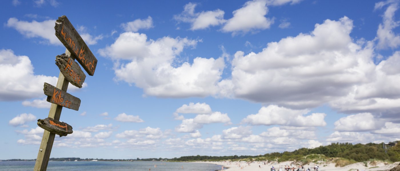 Sandstrand vid havet med en vägvisande skylt i förgrunden