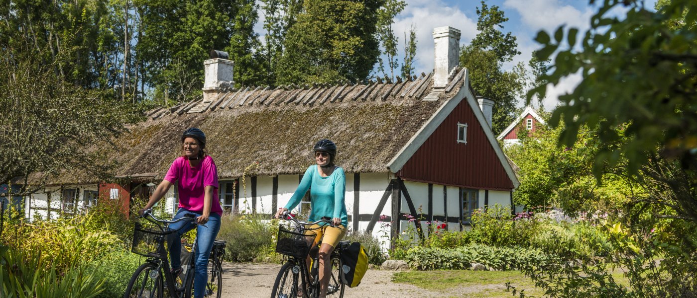 två personer cyklar på en väg framför ett hus
