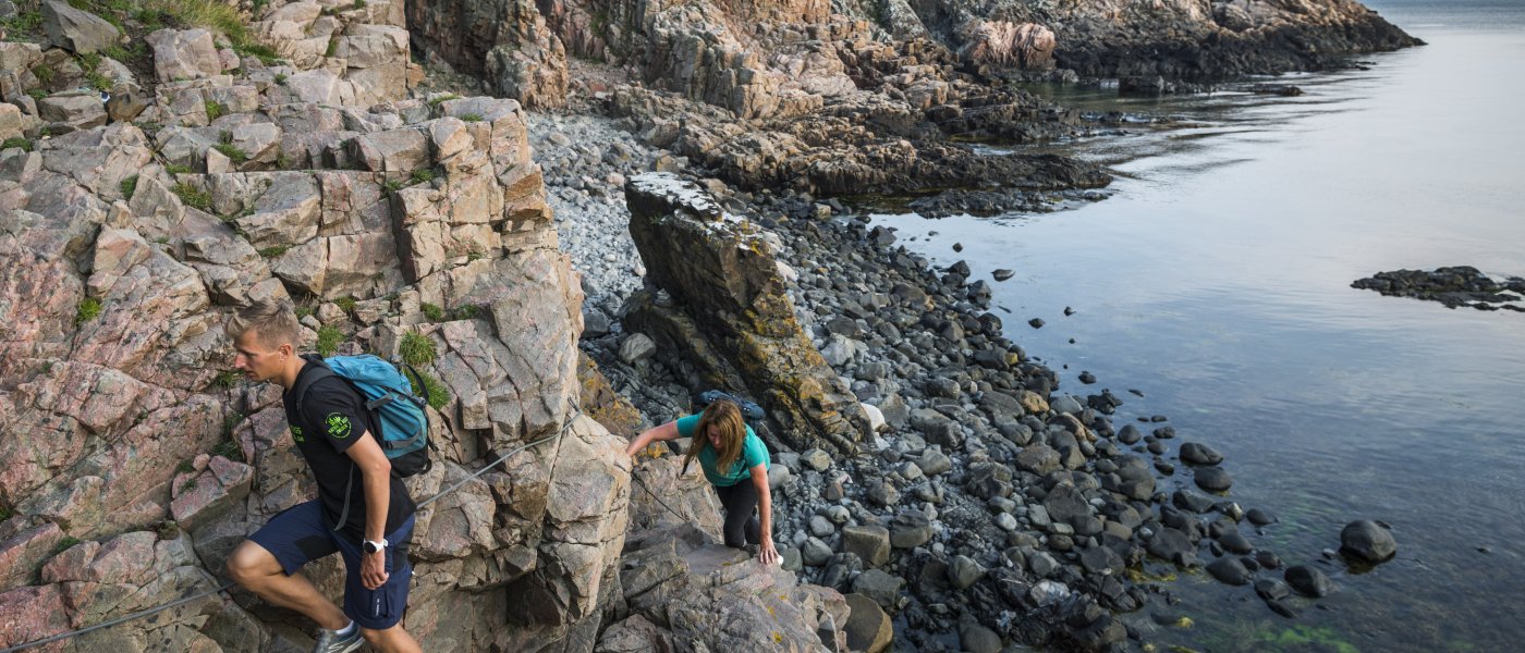 Två personer klättrar på klippor vid vatten