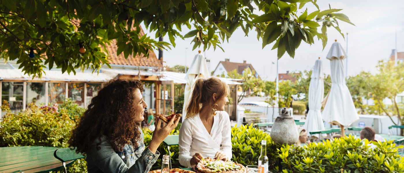 Två kvinnor fikar på café i grönska