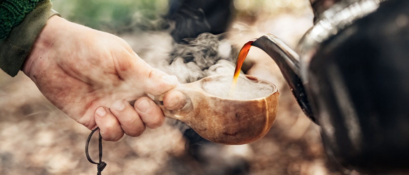 Rykande hett kaffe hälls upp i en träkåsa ute i naturen