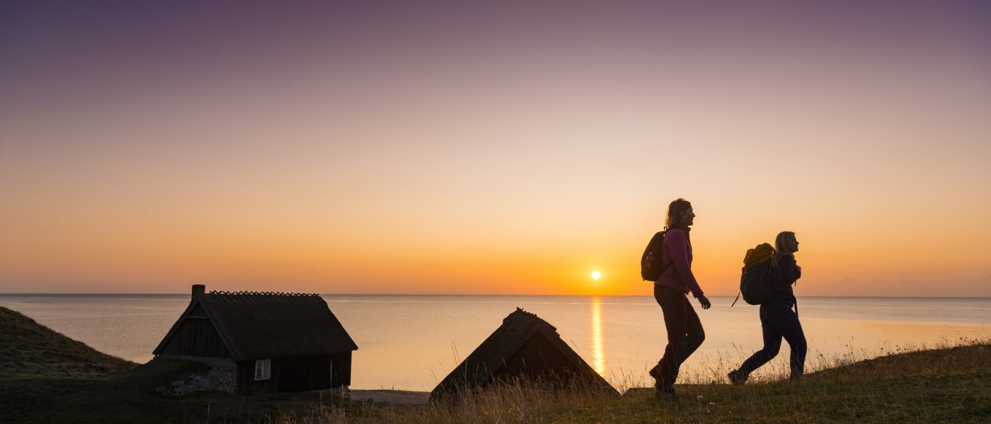 Siluetter av två vandrare vid havet i solnedgång. Foto.