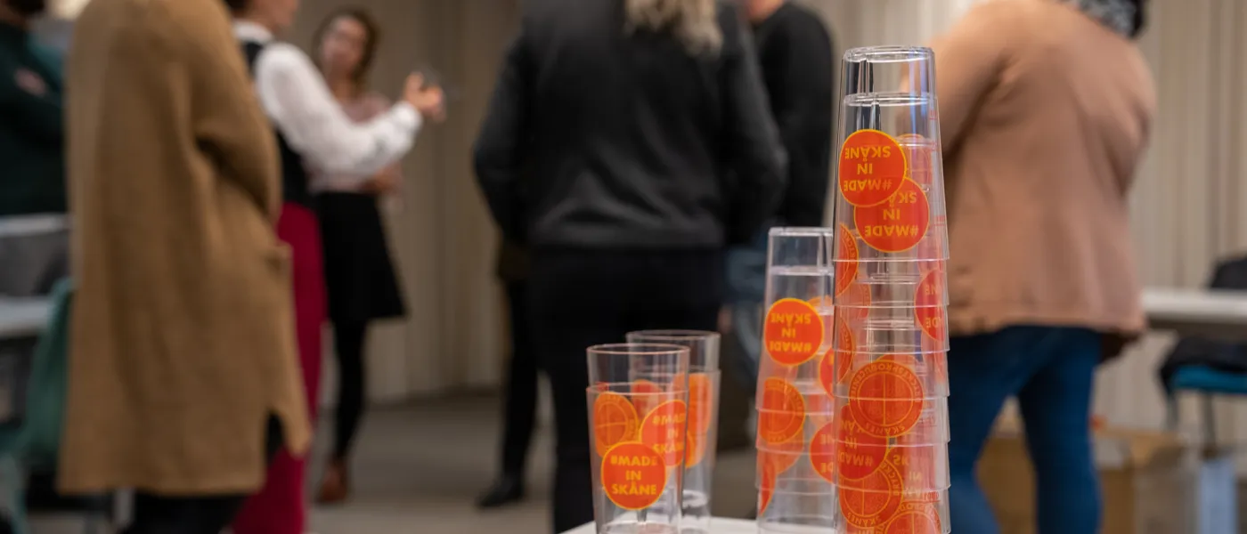 Glas märkta med #Made in Skåne i förgrunden. I bakgrunden står specialistteamet och diskuterar. Foto.