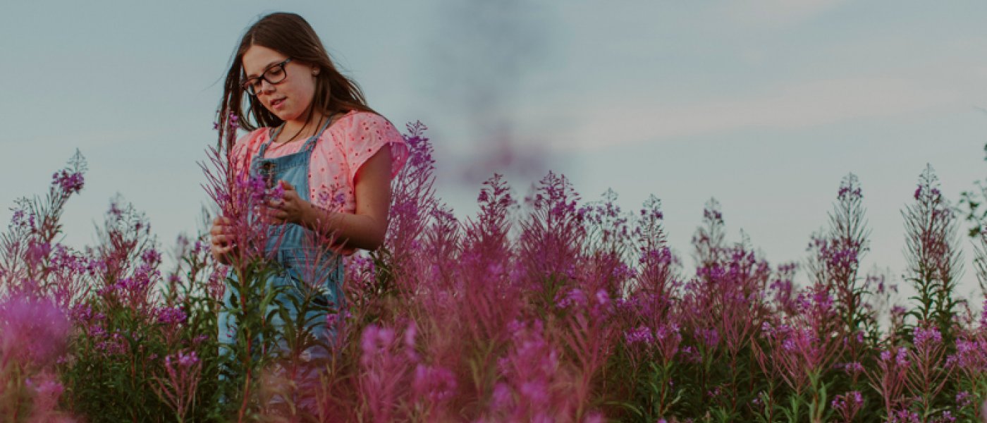 En flicka står på en äng med rosa blommor. Foto.