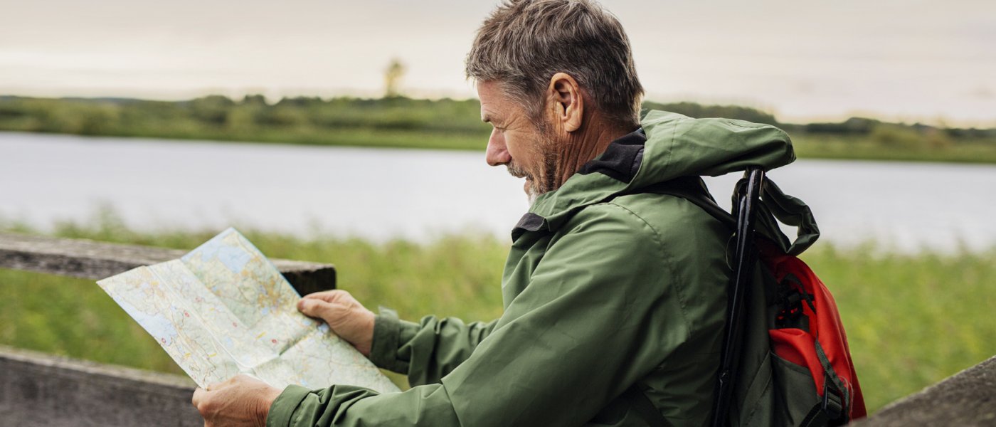 En man läser en karta ute i naturen. Foto.