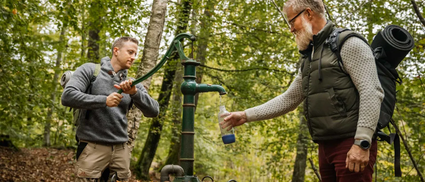 Två män pumpar vatten i skogen
