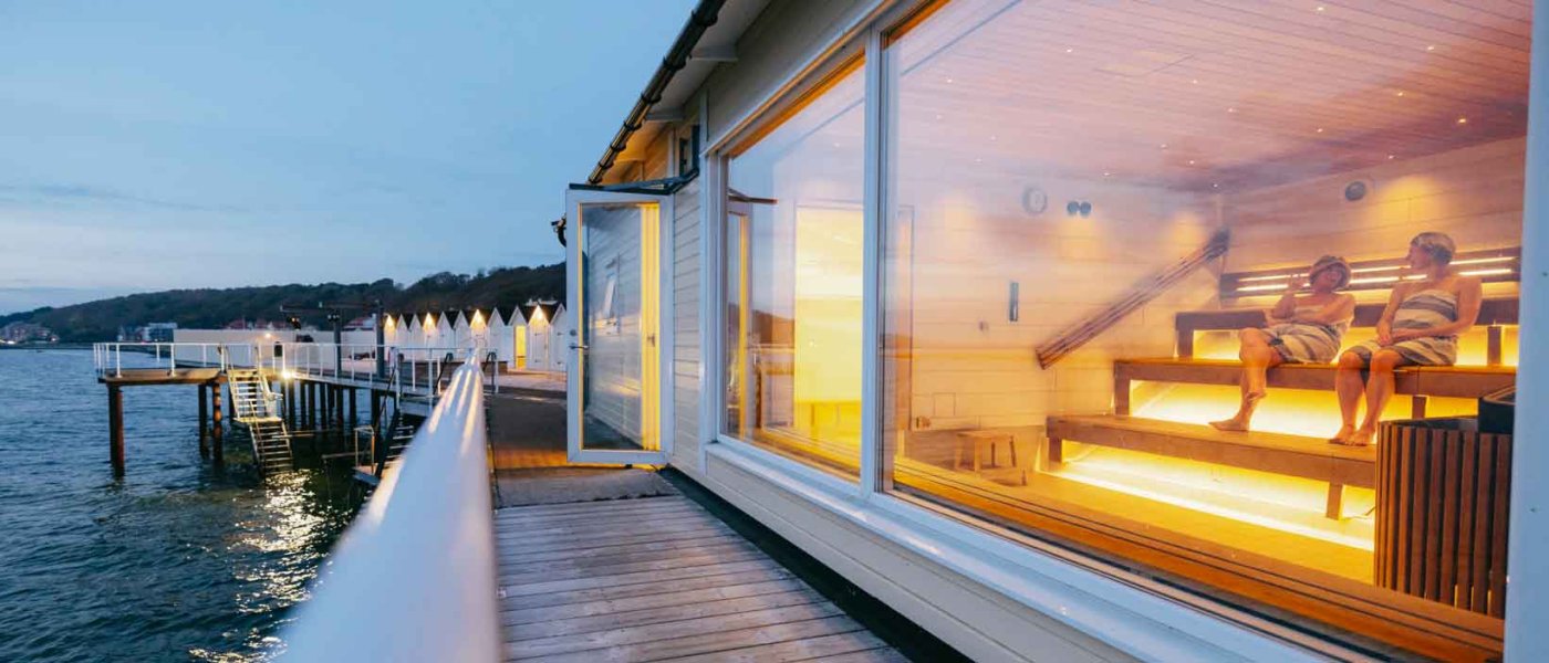 Brygga och stort fönster vid bastu med två kvinnor i randiga handdukar