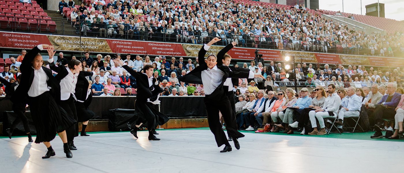 Svartklädda dansare på ett vitt blankt dansgolv framför en stor scen