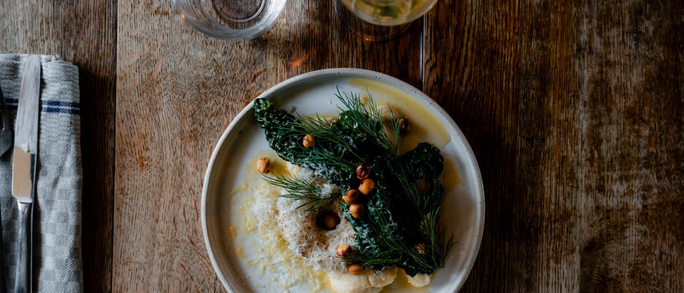 Dukning på mörkt träbord sedd uppifrån med tallrik med puré, svartkål och hasselnötter