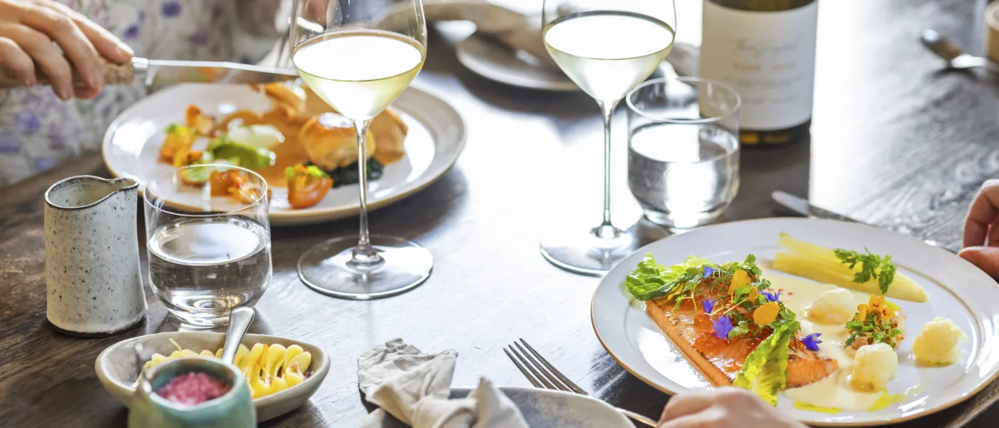 Uppdukat bord på nära håll där två personer äter en fin middag och dricker vitt vin