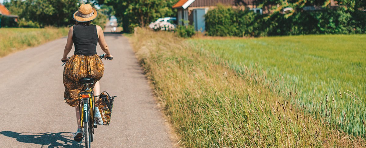 Kvinna cyklar på Ven en solig sommardag. Foto.