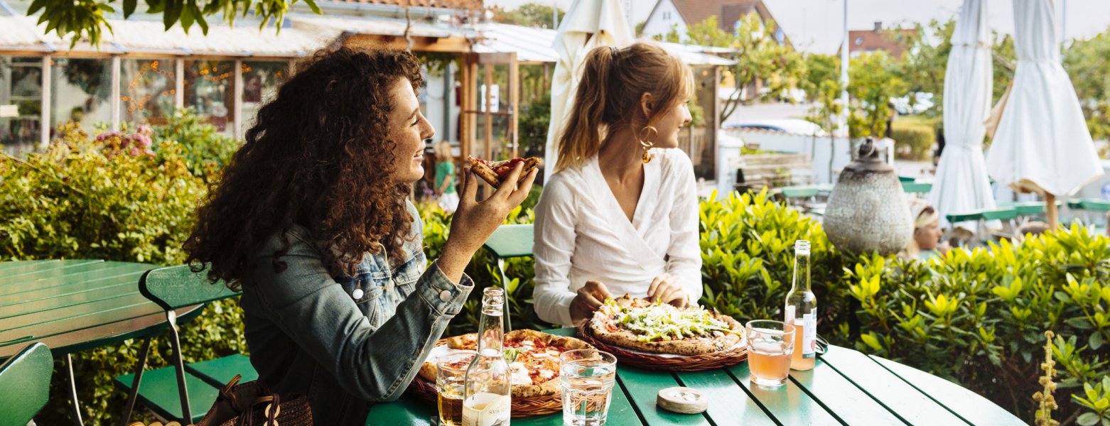 Två kvinnor äter pizza på en uteservering. Foto.