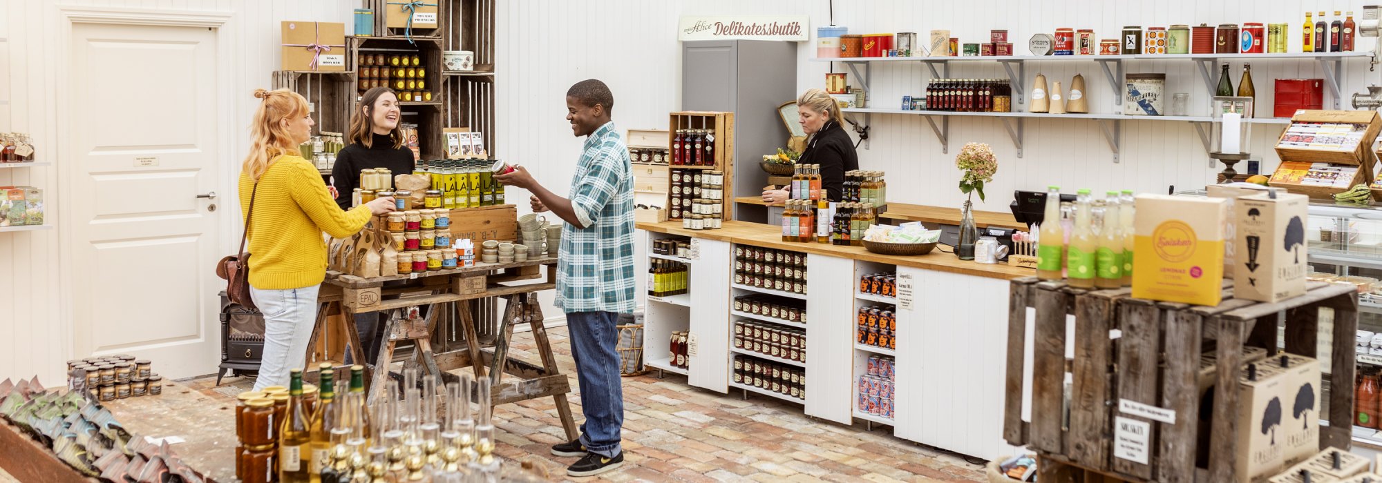 Tre personer står runt ett bord med produkter i en gårdsbutik. Foto.