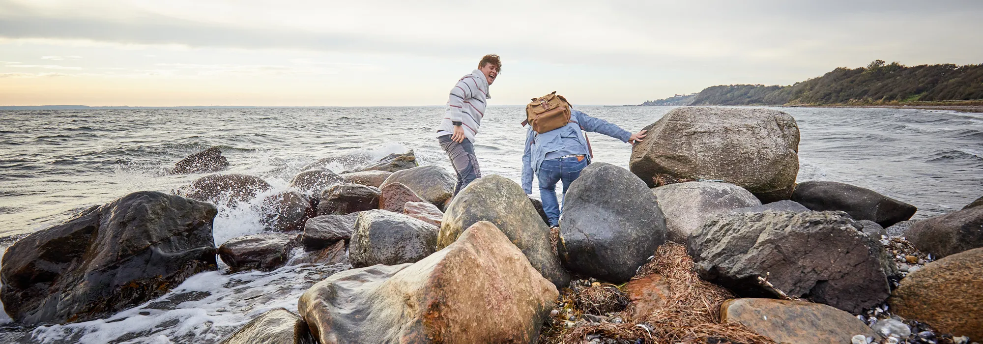 Två personer klättrar på stenar vid havet. Foto.