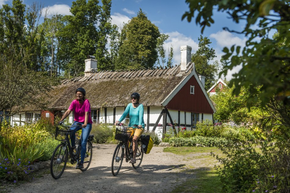 två personer cyklar på en väg framför ett hus