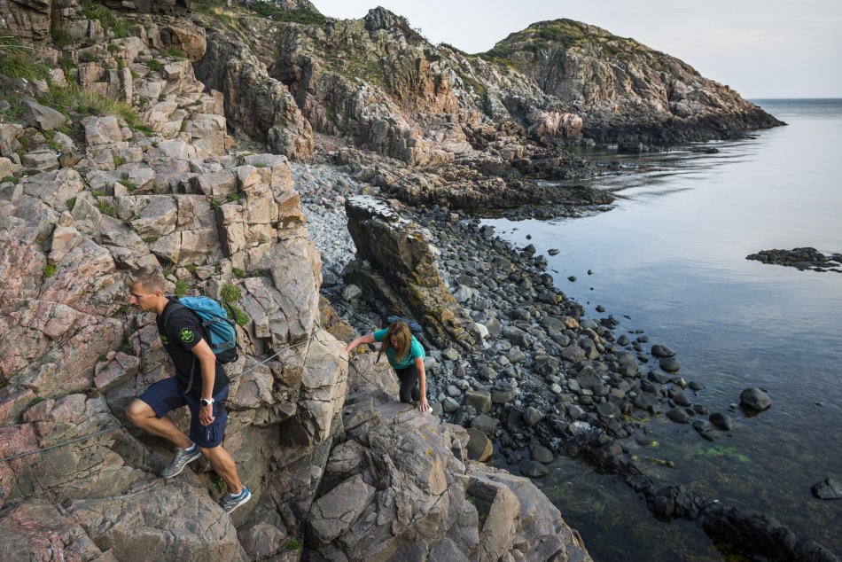 Två personer klättrar på klippor vid vatten