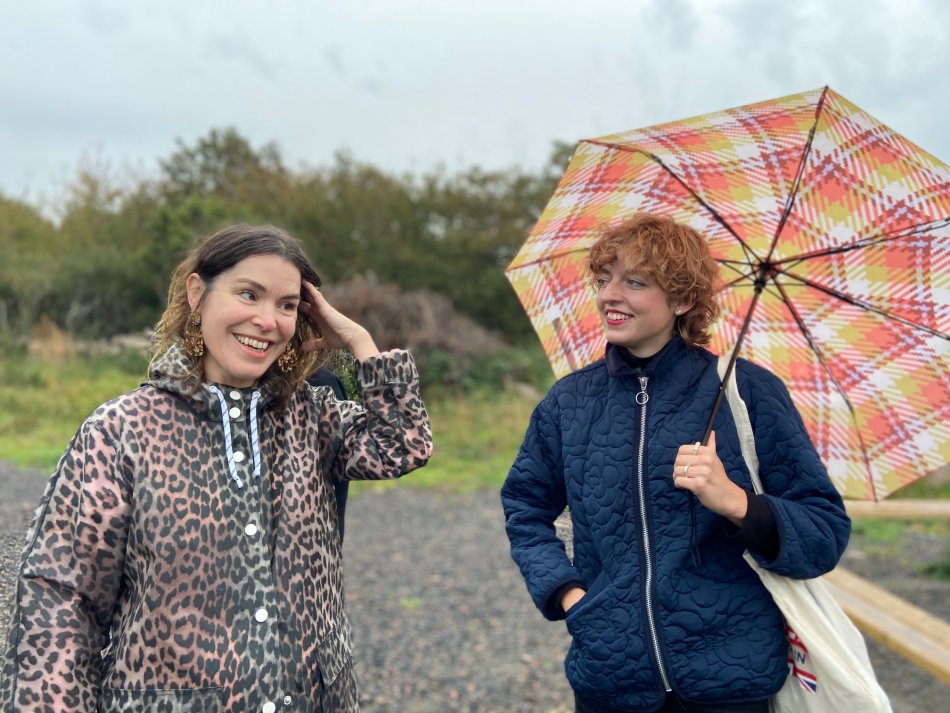 Designerduon "Henriksson och Lindgren" står utomhus en regnig dag med regnkläder och paraply.