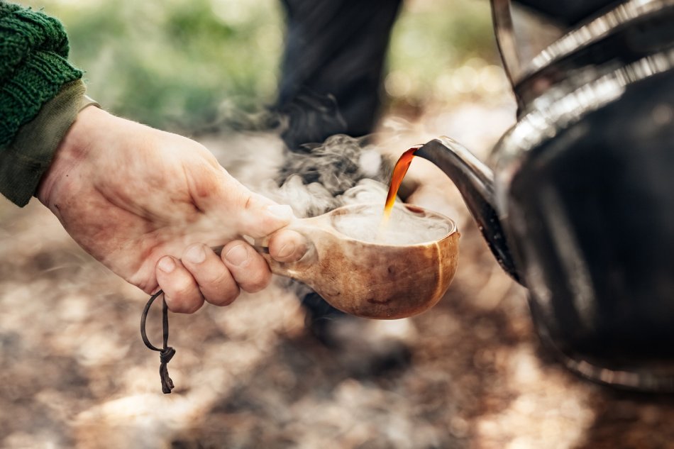Rykande hett kaffe hälls upp i en träkåsa ute i naturen