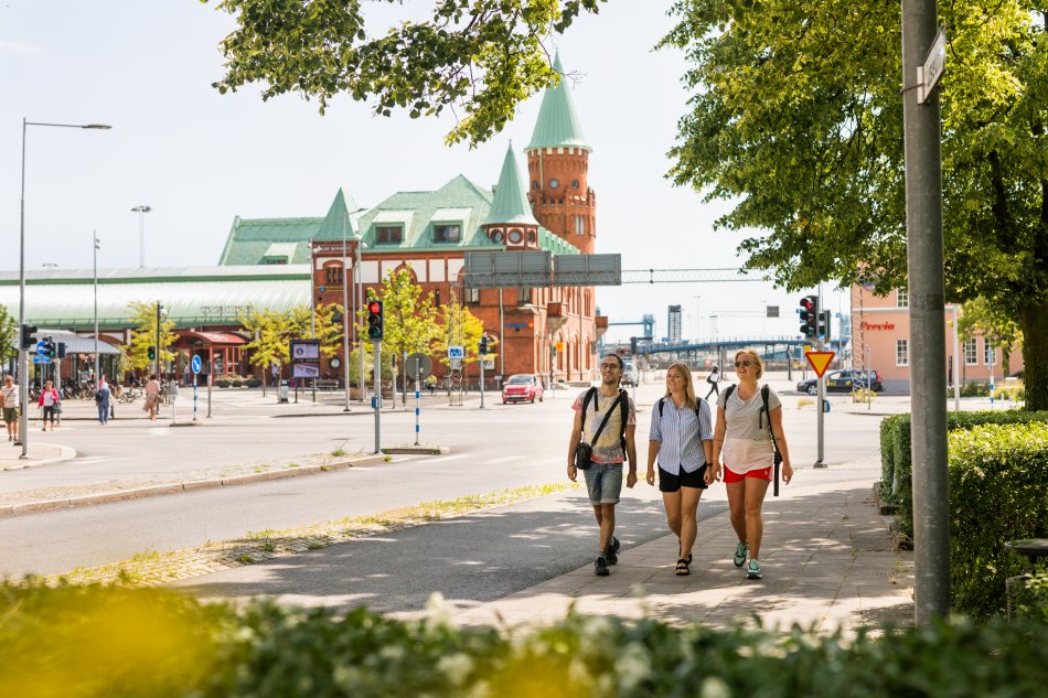 Tre personer promenerar i grönskande stad