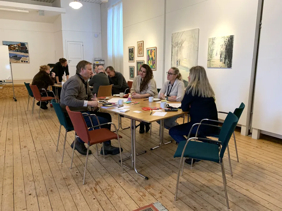 Deltagare från Pop Upp sitter vid två bord och pratar med varandra. Foto.