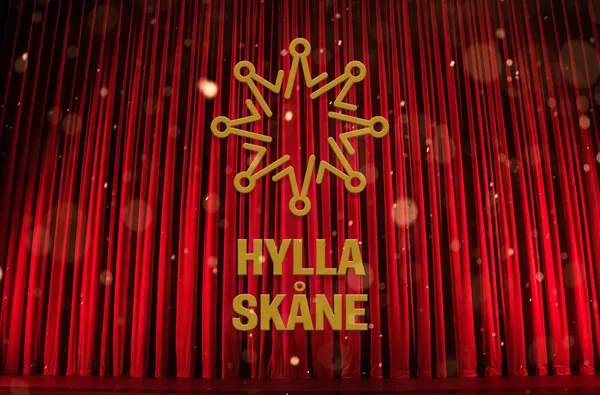 Hylla Skåne logotyp mot en ridå på scen. Foto.