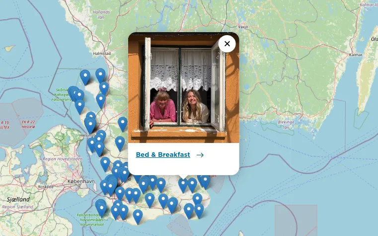 Karta över upplevelser i Skåne utmärkta med kartnålar. En kartnål är markerad och visar att det är för ett Bed and breakfast med bild på två kvinnor som tittar ut genom ett fönster. 