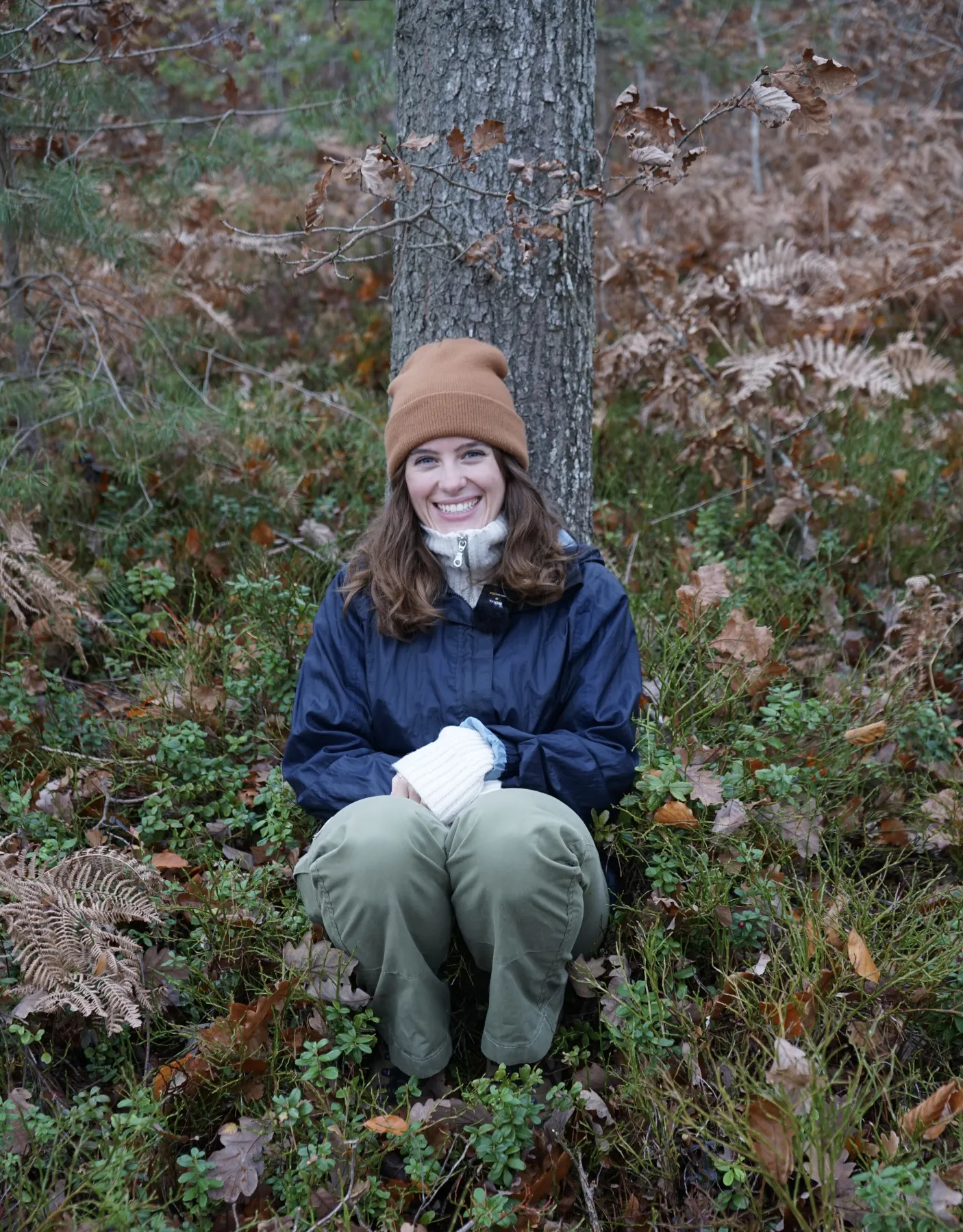 Ellen sitter med ryggen mot en trädstam i skogen. 