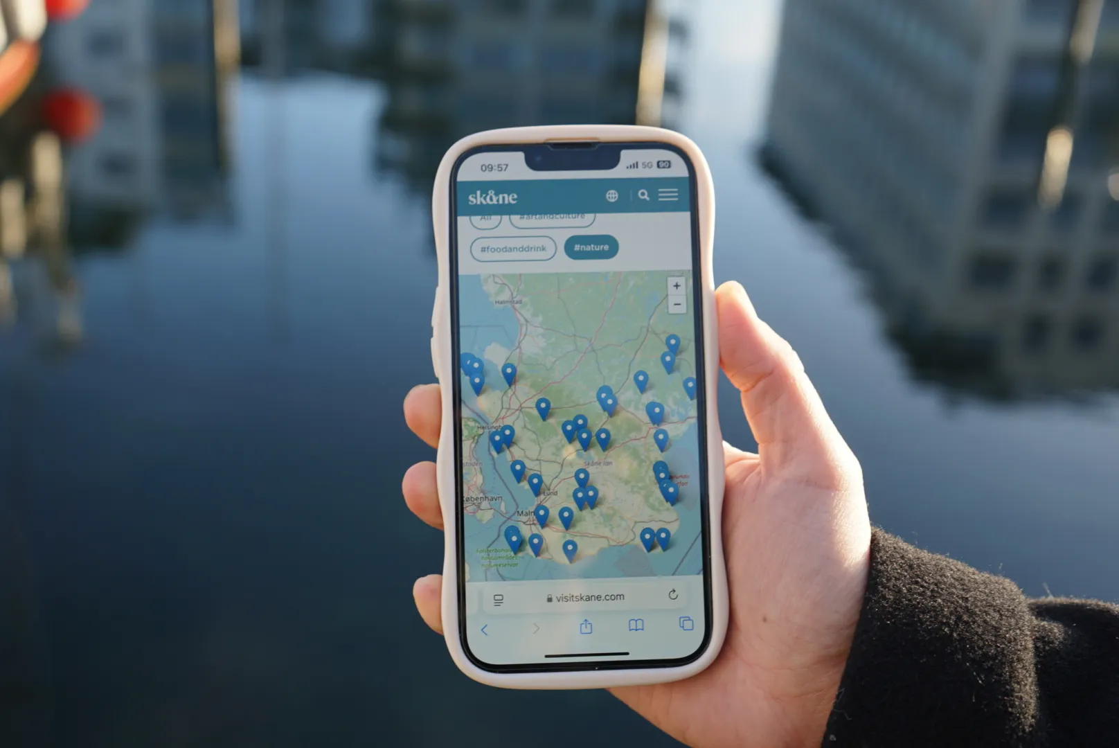 En hand håller en mobiltelefon som visar upp en karta över Skåne utmärkt med kartnålar.